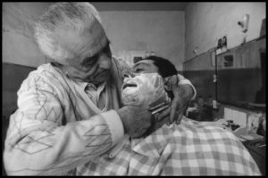 BARBERS OF SICILY Patti (Messina) 1992. Il barbiere… di fiducia. Meglio mettersi nelle mani di Figaro che in quelle di Ippocrate. Ma è bene avere i conti a posto. Può scappare la mano. C’è poi la moglie del tonsor che sta cercando la tovaglia da tavola. Qualcuno ne sa qualcosa?